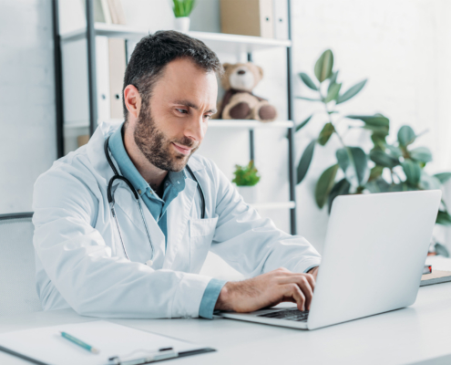 Positive doctor sitting at workplace and using laptop