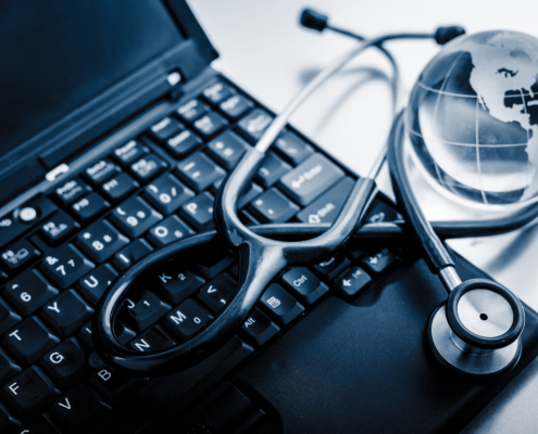 Top down view of a stethoscope and globe laying on top of a laptop keyboard